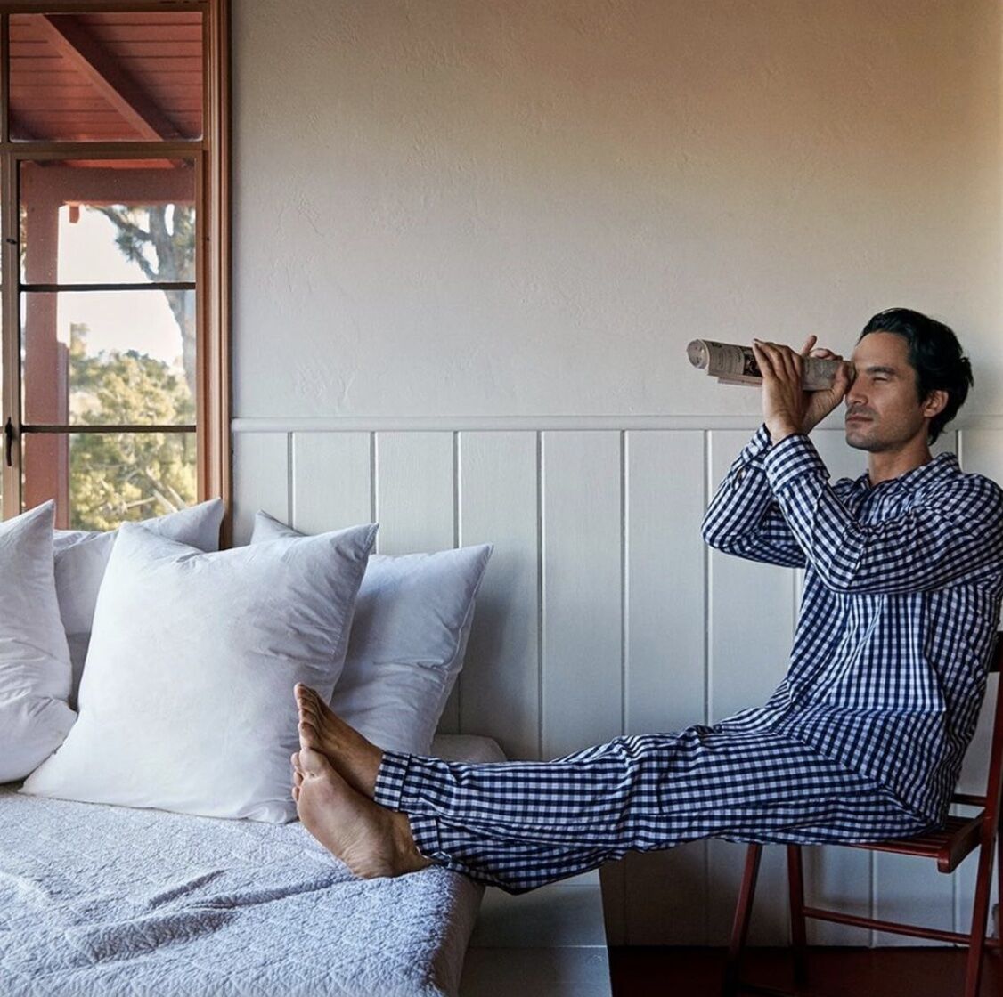 man in pajama set sitting beside the best with a rolled up newspaper looking through it like a telescope